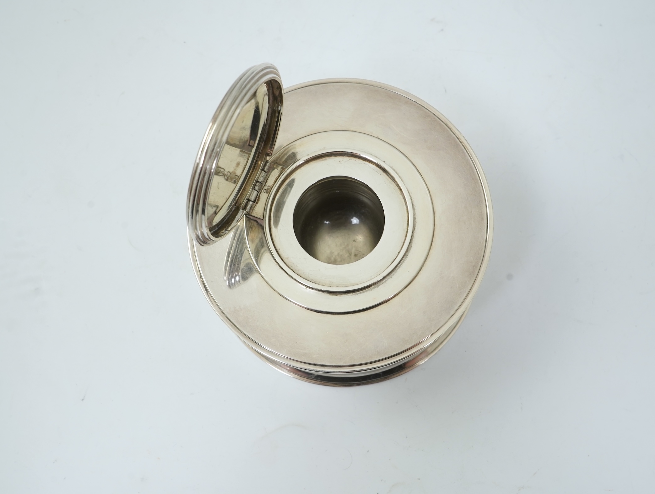 A George V silver circular inkwell, by Sebastian Garrard, commemorating the Silver Jubilee of King George V, the die stamped cover designed by George Kruger Gray featuring the Goldsmiths Company Coat of Arms